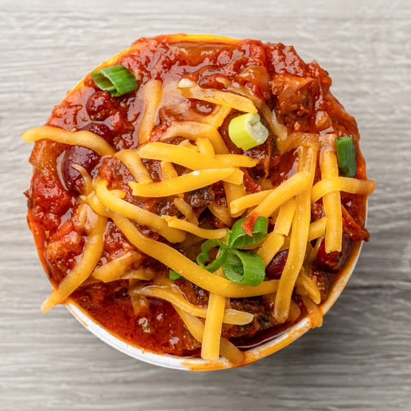 Hawg Jaw Que & Brew's chili with shredded cheese and green onions in a white bowl.