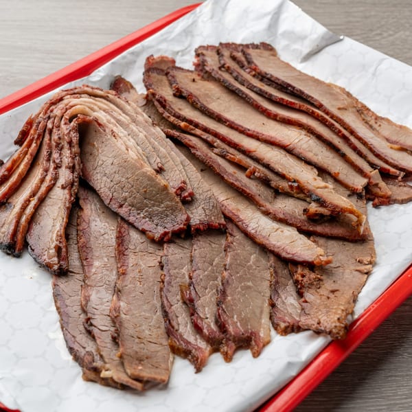 Close-up of thinly sliced Hawg Jaw Que & Brew brisket on white paper in a red tray.