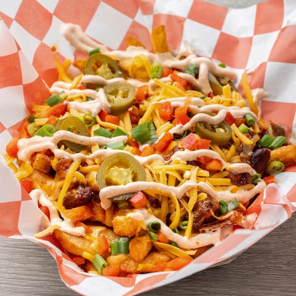 Hawg Jaw Que & Brew's loaded fries with cheese, jalapeños, tomatoes, green onions, and sauce in a basket.