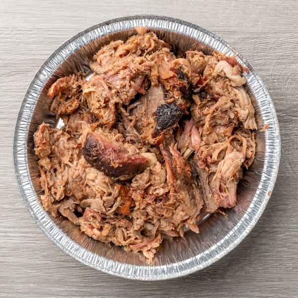 Hawg Jaw Que & Brew's pulled pork in a silver foil takeout container on a wooden surface.