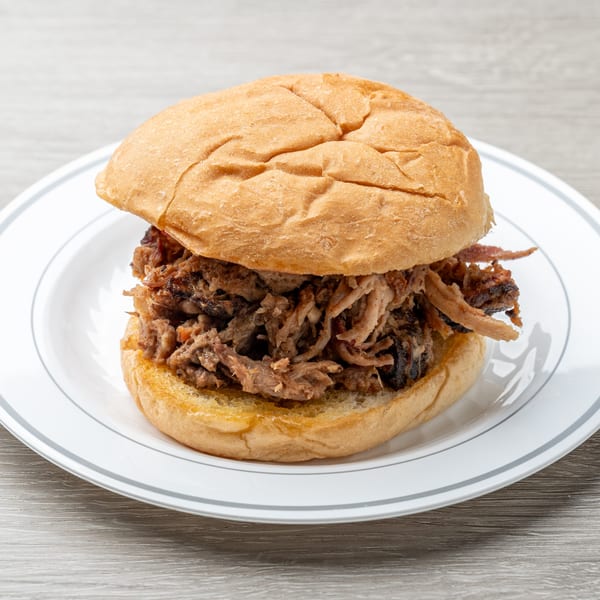 A Hawg Jaw Que & Brew pulled pork sandwich on a white plate with a grey stripe.