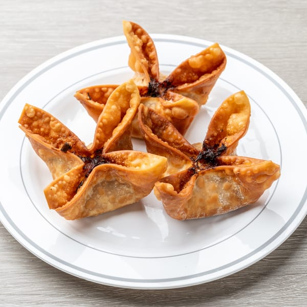 Four golden-brown, star-shaped fried wontons with dark filling on a white plate.